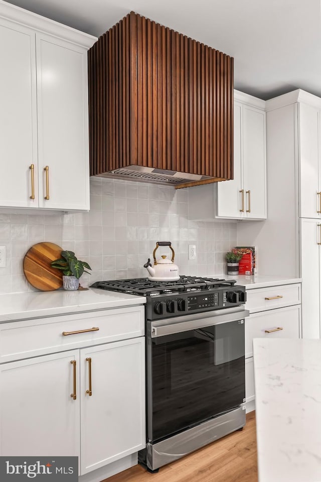 kitchen with white cabinetry, light wood-type flooring, tasteful backsplash, and stainless steel gas range oven