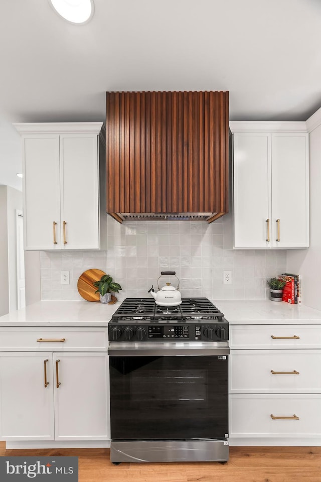 kitchen featuring tasteful backsplash, premium range hood, gas range oven, white cabinets, and light hardwood / wood-style flooring