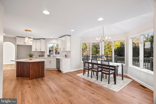 kitchen with a kitchen island, white cabinetry, hanging light fixtures, light wood-type flooring, and stainless steel dishwasher