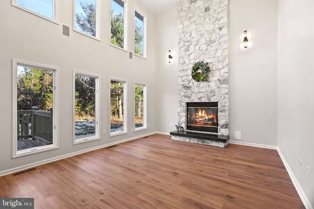 unfurnished living room featuring hardwood / wood-style floors, a towering ceiling, and a stone fireplace