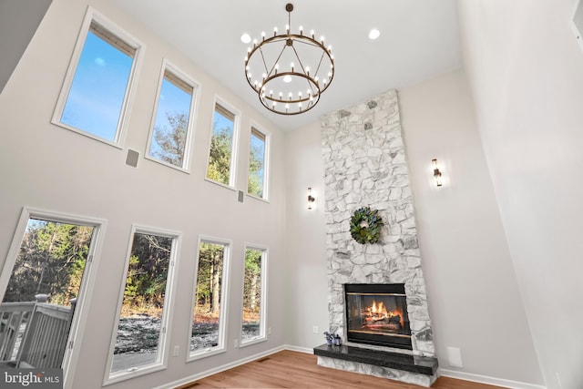 living room with hardwood / wood-style flooring, an inviting chandelier, a towering ceiling, and a fireplace