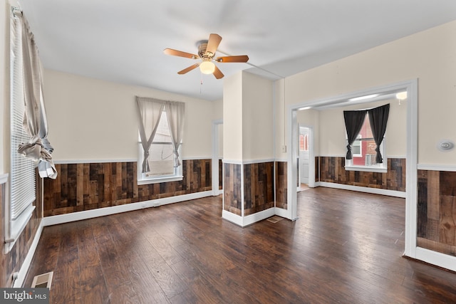 empty room with ceiling fan, wood-type flooring, and wood walls