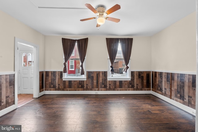 spare room featuring dark wood-type flooring, ceiling fan, and wood walls