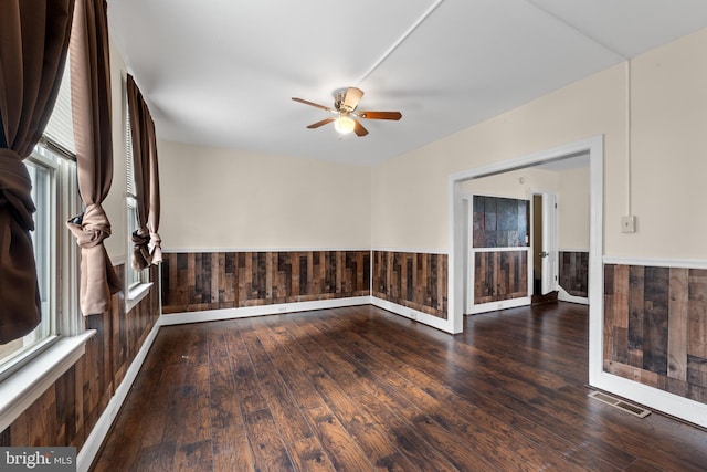 spare room with dark wood-type flooring, wooden walls, and a wealth of natural light