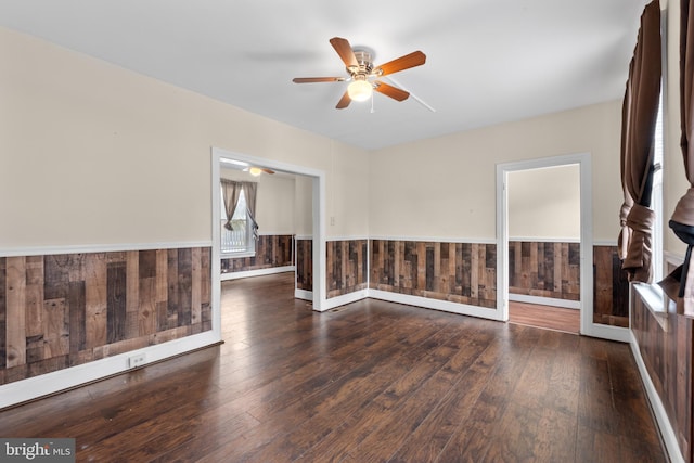 empty room featuring dark wood-type flooring, wooden walls, and ceiling fan