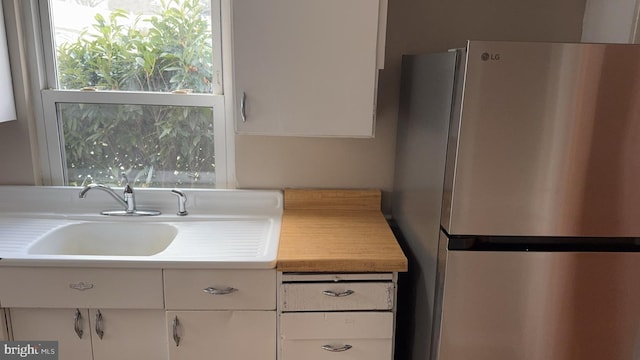 kitchen featuring stainless steel refrigerator, white cabinetry, and sink