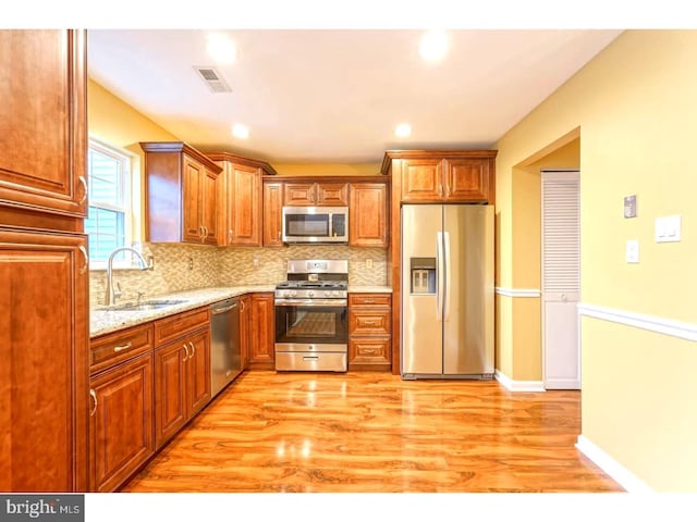 kitchen featuring appliances with stainless steel finishes, sink, backsplash, light stone counters, and light wood-type flooring