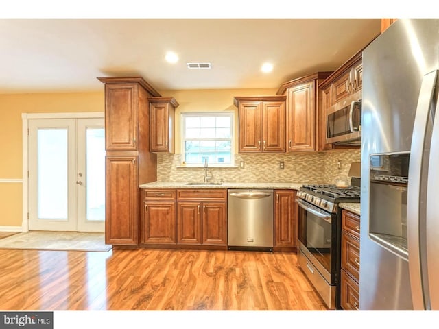 kitchen with sink, tasteful backsplash, light stone counters, stainless steel appliances, and light hardwood / wood-style floors