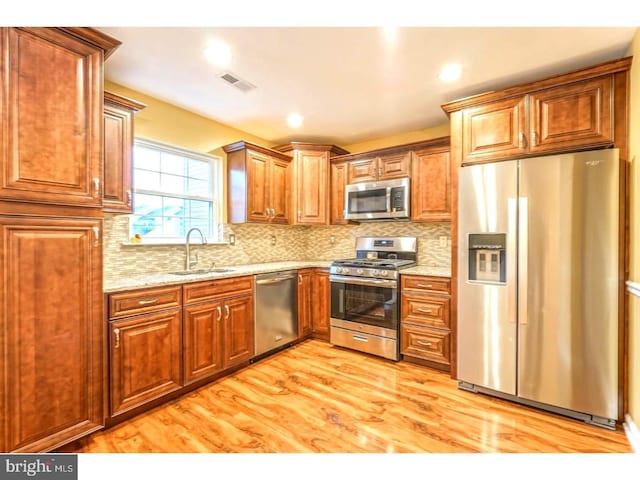 kitchen featuring appliances with stainless steel finishes, sink, backsplash, light hardwood / wood-style floors, and light stone countertops