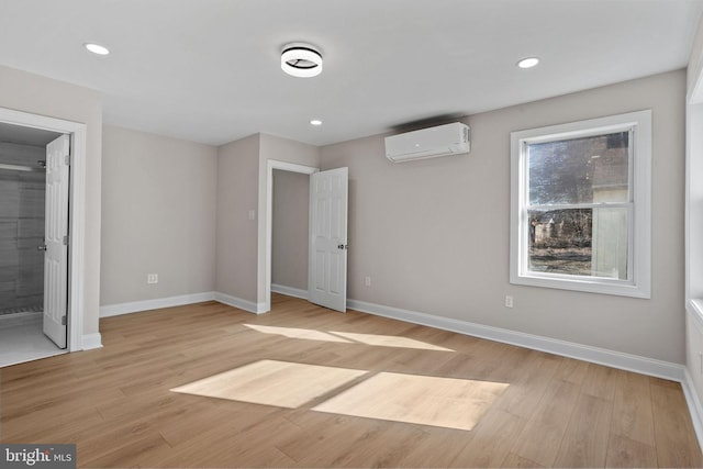 unfurnished bedroom with a wall mounted air conditioner, ensuite bath, and light hardwood / wood-style flooring