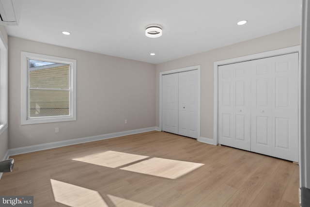 unfurnished bedroom with multiple closets, a wall mounted air conditioner, and light hardwood / wood-style flooring