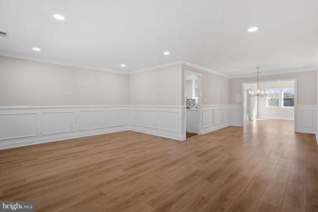 empty room with an inviting chandelier, wood-type flooring, and ornamental molding