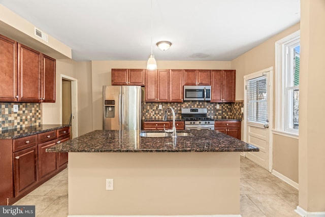 kitchen with sink, a center island with sink, dark stone counters, and stainless steel appliances