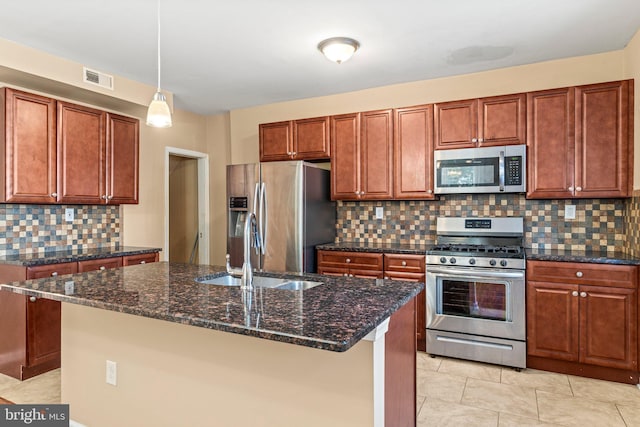 kitchen featuring dark stone countertops, sink, appliances with stainless steel finishes, and an island with sink