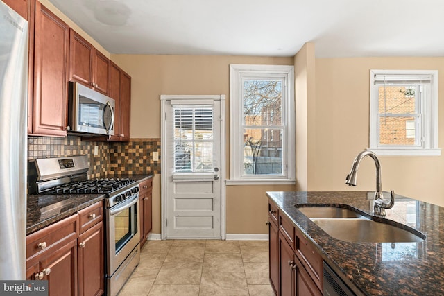 kitchen with sink, stainless steel appliances, dark stone counters, and light tile patterned floors