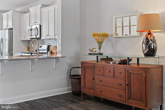 kitchen featuring white cabinetry, a kitchen breakfast bar, dark hardwood / wood-style flooring, stainless steel appliances, and backsplash