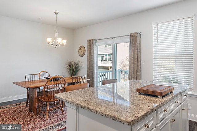 kitchen with light stone counters, a kitchen island, dark hardwood / wood-style flooring, decorative light fixtures, and a chandelier