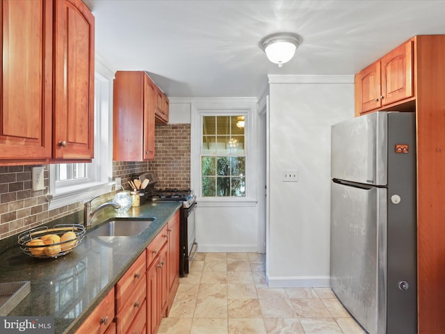 kitchen with sink, stainless steel refrigerator, tasteful backsplash, gas stove, and dark stone counters