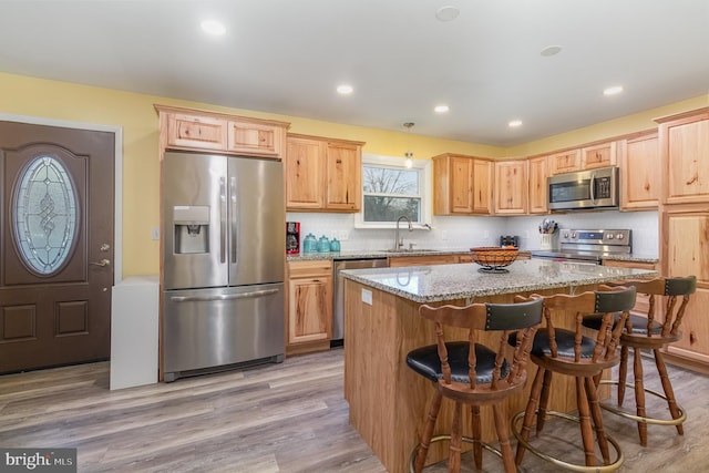 kitchen with a kitchen island, appliances with stainless steel finishes, a kitchen breakfast bar, light hardwood / wood-style floors, and light stone countertops