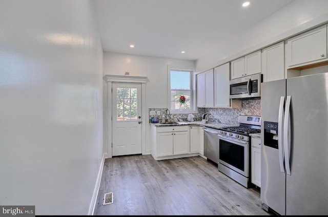 kitchen with white cabinets, appliances with stainless steel finishes, light hardwood / wood-style flooring, and sink