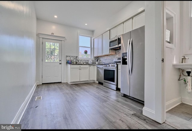 kitchen featuring light hardwood / wood-style floors, white cabinets, backsplash, and appliances with stainless steel finishes