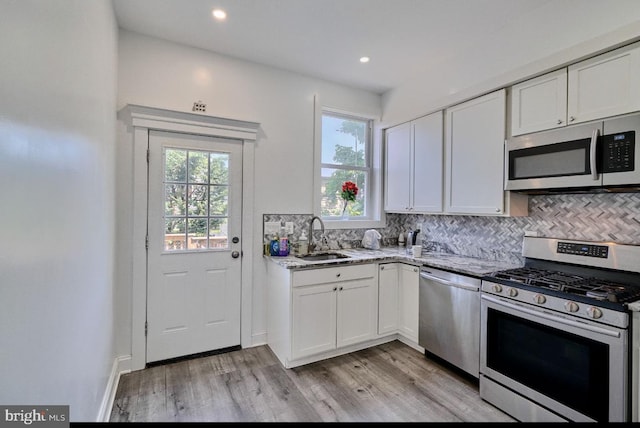 kitchen with sink, white cabinetry, light stone counters, and appliances with stainless steel finishes