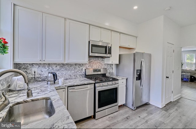 kitchen featuring light stone countertops, white cabinetry, stainless steel appliances, sink, and backsplash