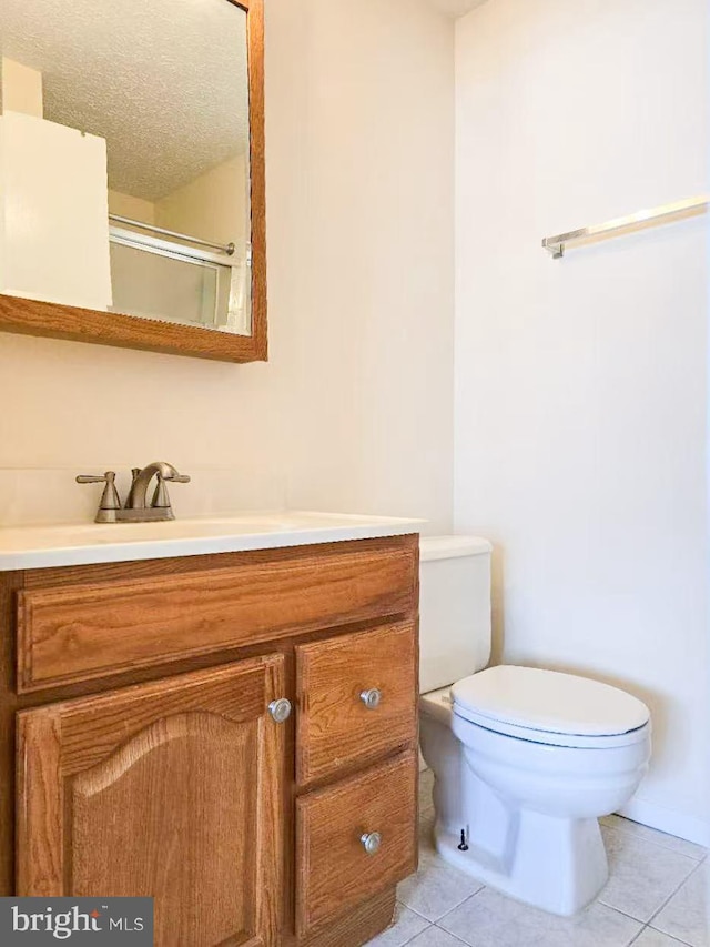 bathroom with a shower with door, vanity, tile patterned floors, and toilet