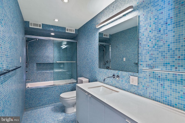 full bathroom featuring toilet, combined bath / shower with glass door, tile walls, tile patterned flooring, and vanity