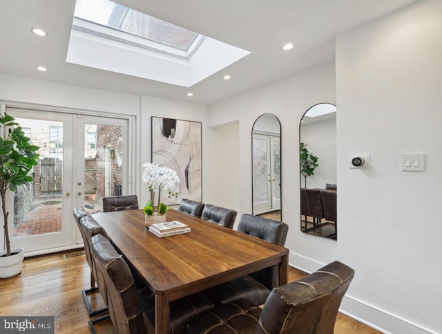 dining space with hardwood / wood-style flooring, a skylight, and french doors