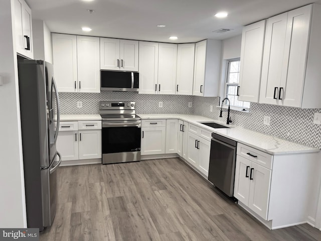 kitchen with appliances with stainless steel finishes, tasteful backsplash, sink, white cabinets, and light wood-type flooring