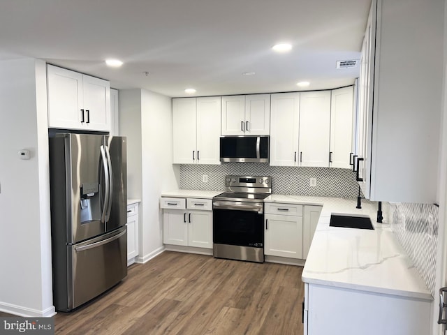 kitchen with sink, appliances with stainless steel finishes, dark hardwood / wood-style floors, light stone countertops, and white cabinets