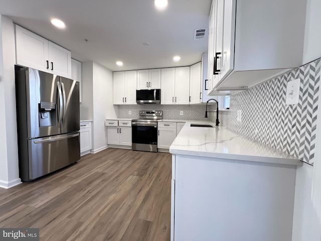 kitchen with appliances with stainless steel finishes, sink, white cabinets, light stone counters, and dark wood-type flooring