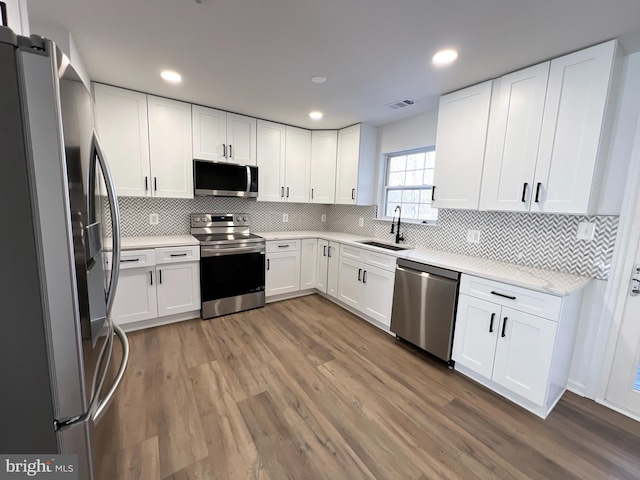 kitchen with appliances with stainless steel finishes, white cabinetry, sink, decorative backsplash, and hardwood / wood-style flooring