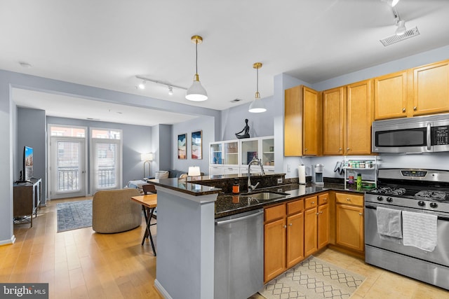 kitchen with pendant lighting, sink, stainless steel appliances, kitchen peninsula, and dark stone counters