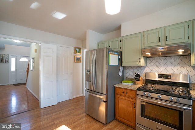 kitchen with light stone counters, appliances with stainless steel finishes, light hardwood / wood-style floors, and decorative backsplash