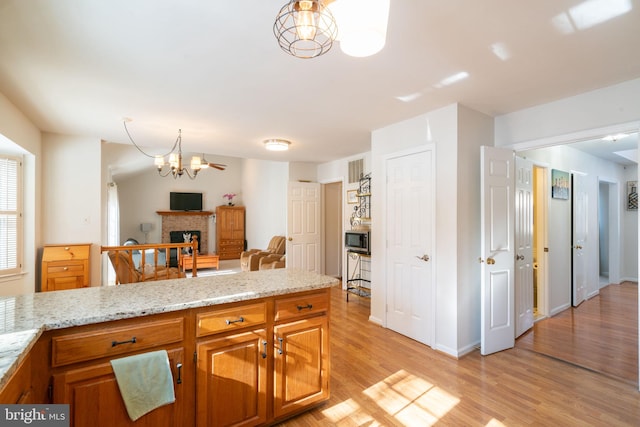 kitchen featuring stainless steel microwave, a fireplace, light wood-type flooring, light stone countertops, and an inviting chandelier