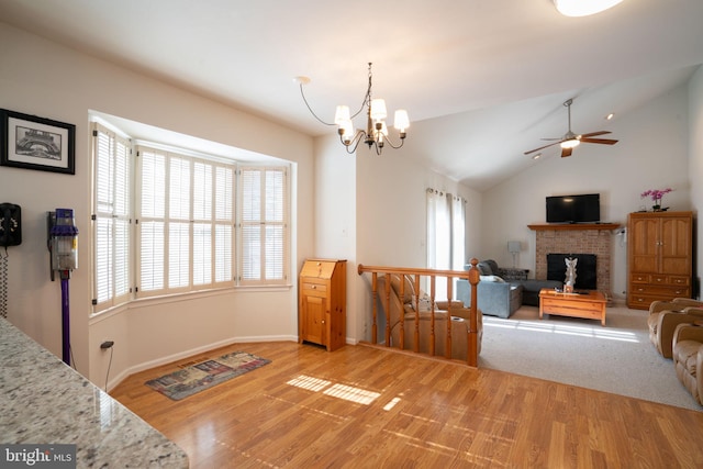 interior space with lofted ceiling, ceiling fan with notable chandelier, a fireplace, and light hardwood / wood-style floors