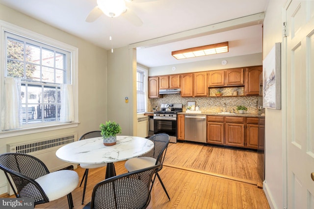 kitchen with radiator heating unit, sink, decorative backsplash, stainless steel appliances, and a healthy amount of sunlight