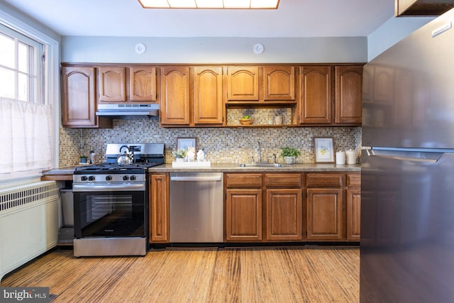 kitchen featuring radiator, sink, backsplash, light hardwood / wood-style floors, and stainless steel appliances