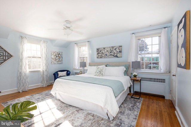 bedroom with dark wood-type flooring, ceiling fan, radiator heating unit, and multiple windows