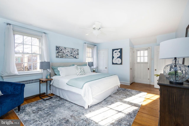 bedroom with multiple windows, radiator, wood-type flooring, and ceiling fan