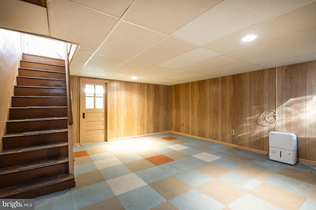 basement featuring a drop ceiling and wooden walls