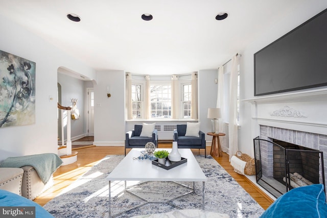 living room featuring radiator heating unit, light hardwood / wood-style floors, and a brick fireplace