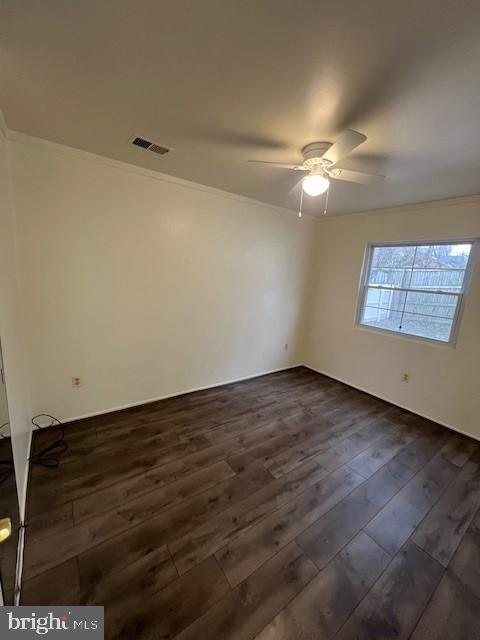 empty room with dark wood-style floors, a ceiling fan, visible vents, and crown molding