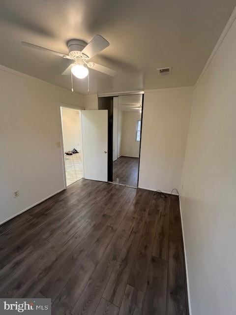 unfurnished bedroom featuring dark wood-style floors, a closet, visible vents, ornamental molding, and ceiling fan