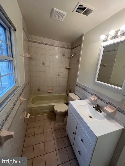 bathroom with shower / bathing tub combination, vanity, visible vents, and tile walls