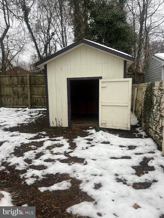 snow covered garage featuring a garage, fence, and a shed