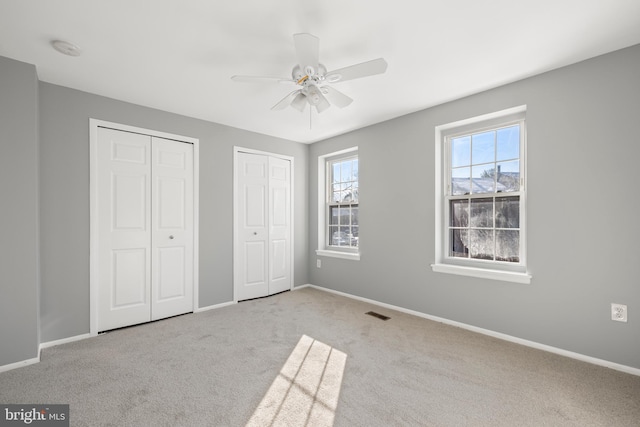 unfurnished bedroom with light carpet, two closets, and ceiling fan