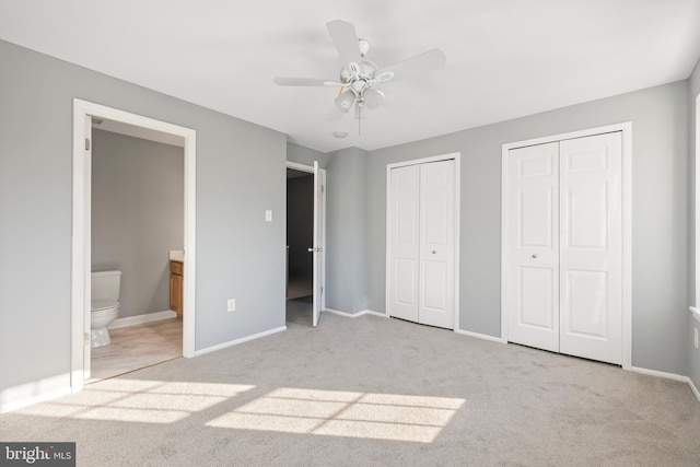 unfurnished bedroom with light carpet, connected bathroom, two closets, and ceiling fan